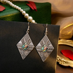 Close-up of bohemian diamond-shaped earrings with vintage silver engraving and shell inlay