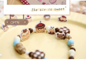 Close-up of beaded bracelet with strawberry cake and bear charms on a dessert plate