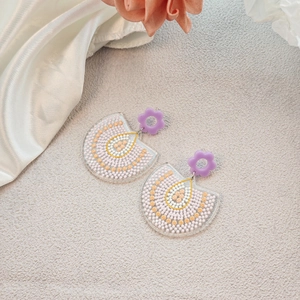 Detail of floral earrings with purple flower studs and colorful spotted acrylic drops