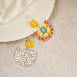 Detail of bohemian acrylic fan earrings with yellow flower studs on a white silk cloth