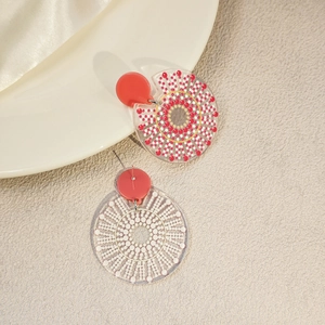 Detailed close-up of asymmetric resin earrings featuring red and white artistic dot patterns