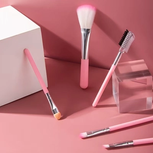 Five-piece pink makeup brush set with matte handles and soft bristles on minimalist backdrop