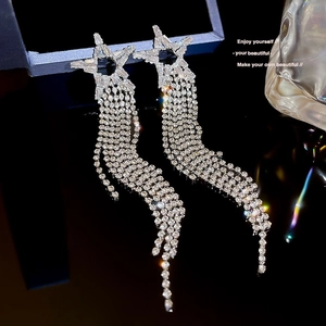 Silver dangling earrings with star-shaped zircons and long tassels on black mirror