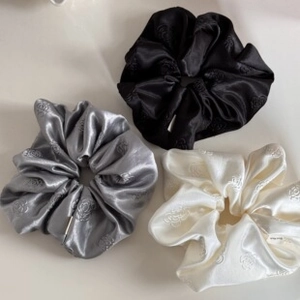 Detailed view of satin scrunchies with floral texture in black, grey, and cream colors