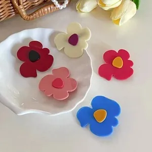 Close-up of matte resin flower hair ties in five vibrant colors on a white ceramic plate