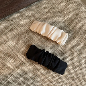 Close-up of elegant pleated satin hair clips in black and creamy white fabric texture