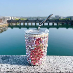 Close-up of pink rhinestone insulated straw cup with peacock motif and pearl accents