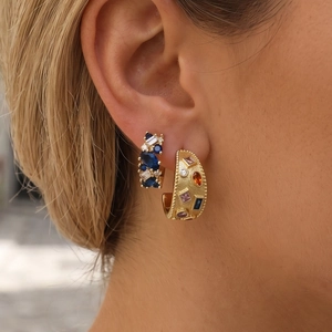 Close-up of matte gold earrings with blue crystals and multi-color gemstones on ear