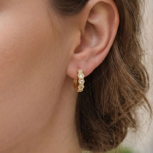 Close-up of gold hexagonal honeycomb huggie earrings with round zircons on a model