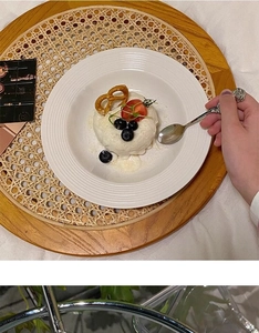 White ceramic plate with embossed edges on a woven rattan tray with a rose silver spoon