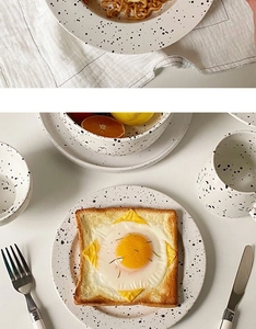 Close-up of minimalist ink-splatter ceramic plates and mugs on white linen napkins