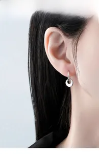 Close-up of minimalist silver disc drop earrings worn by a model in a studio setting
