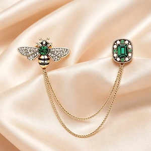 Vintage golden bee brooch with green emerald gems and twin tassel chains on satin