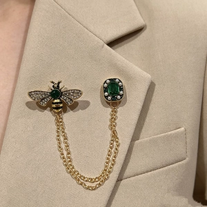 Vintage gold bee chain brooch with emerald gemstone and pearls on a beige blazer