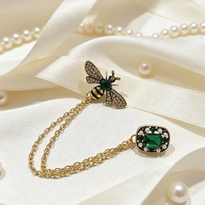 Detailed close-up of vintage bee chain brooch with green gems and pearls on white silk