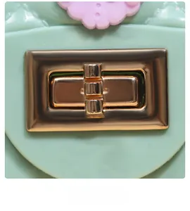 Close-up of golden rectangular twist lock and purple flower on mint green mini bag