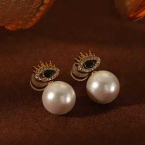 Detail of eye-shaped pearl earrings with gold lashes and a black gemstone inlay