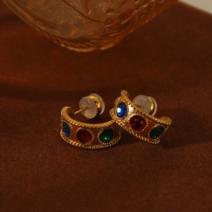 Detail of vintage gold hoop earrings with multi-colored gemstones on leather