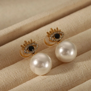 Macro shot of gold Evil Eye pearl earrings with zircon inlay on beige fabric base
