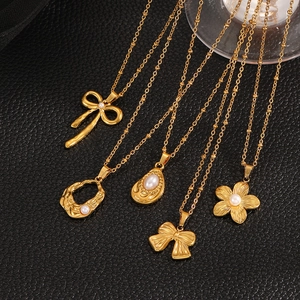 Detail view of five gold-plated pendant necklaces with bows and pearls on black leather