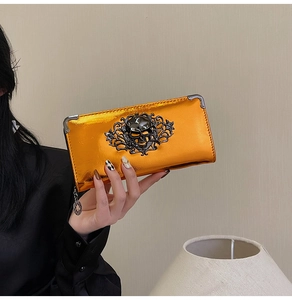 Close-up of vibrant orange metallic wallet with gothic skull relief and floral metal decor