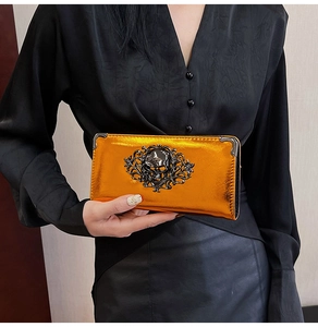 Detail view of metallic orange skull wallet held by hand showing large metal skull and filigree