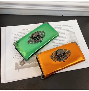 Glossy green and metallic orange long skull wallets with floral metal clasps on a magazine