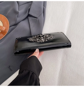 Detail of glossy black skull wallet with gothic relief patterns and metal corners