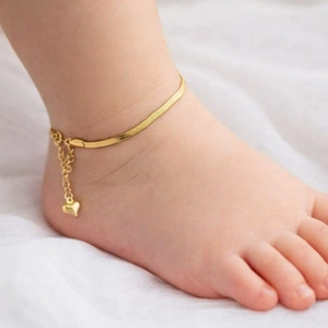 Macro detail of a gold snake chain baby anklet with heart charm on a soft white fabric