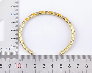 Detail view of 18k gold plated cuff with orange enamel, zircons and size ruler measurement