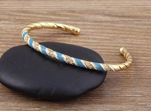 Detail of twisted gold bangle with blue white enamel and sparkling zircon accents