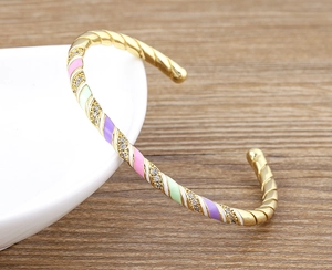Detail of twisted 18k gold plated cuff with colorful enamel segments and small zircon stones