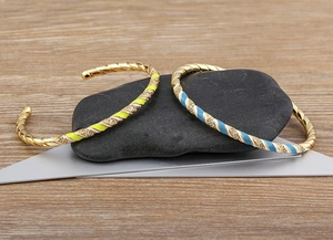 Detail of twisted 18k gold plated bracelets with enamel patterns and white zircon stones