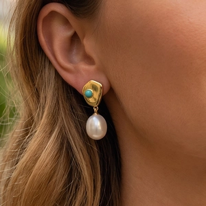 Close-up of vintage gold earrings with turquoise inlay and baroque drop pearl on a model