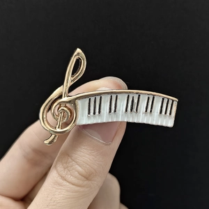 Detail of creative piano keyboard and treble clef music brooch in gold and white enamel