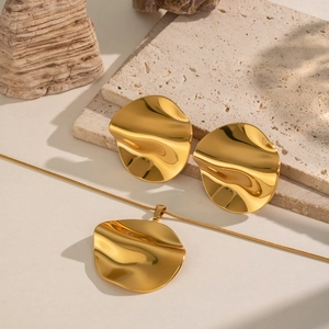 Macro view of irregular wavy gold necklace and earrings set on a travertine stone background