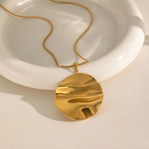 Detail of a large irregular gold pendant on a snake chain over a white ceramic tray