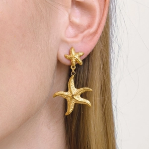 Close-up of golden starfish drop earrings with textured finish on a female model
