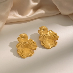 Macro detail of golden lotus leaf earrings with metallic texture on beige silk background