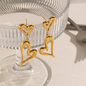 Detail of gold heart-shaped double-layered earrings hanging on a textured glass rim