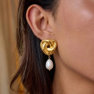 Gros plan sur une boucle d'oreille en métal torsadé doré avec perle d'eau douce blanche