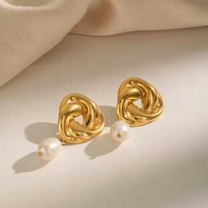 Détail de boucles d'oreilles torsadées dorées avec perles blanches sur tissu beige