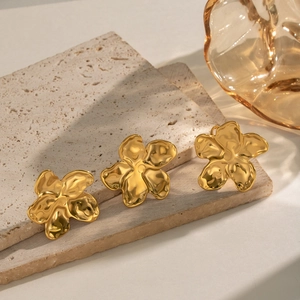 Detailed view of gold flower earrings on stone with elegant ripple texture and shadows