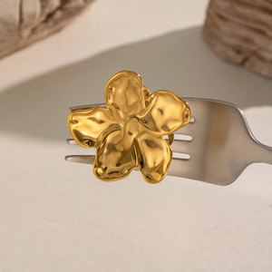 Detail of a golden five-petal flower earring with hammered texture held by a metal fork