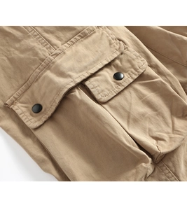 Detailed close-up of khaki cargo pants pocket with double stitching and metal snap buttons