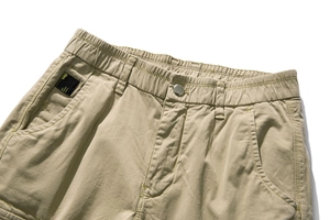 Detail of khaki cargo pants featuring elastic waist, metal button, and branded woven label