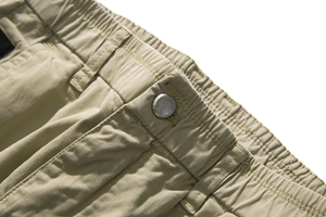 Detailed close-up of light khaki joggers waist with elastic band and silver metal button