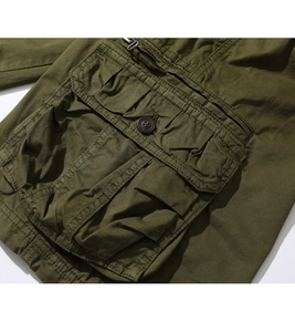 Detail showing tactical cargo pocket with button closure and metallic zipper on green shorts