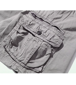 Detail of gray cargo shorts featuring a 3D pocket with flap button and purple zipper