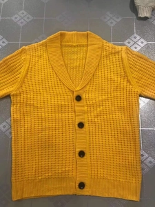 Detailed view of yellow cable-knit cardigan with shawl collar and dark button closures